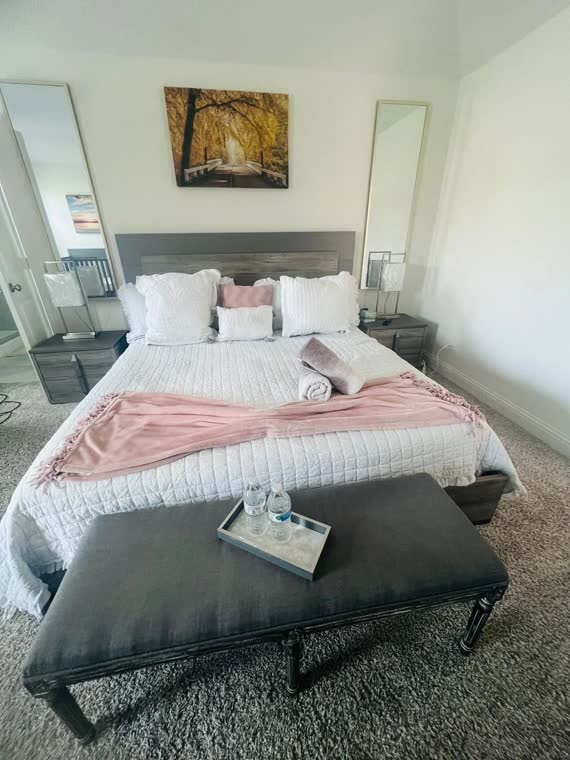 Bedroom with a pink throw, upholstered bench and mirror.